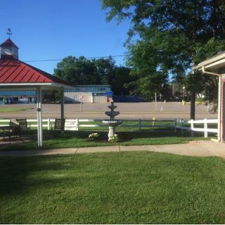 A serene park setting featuring a gazebo, a decorative sculpture, and well-maintained green grass under a clear blue sky.