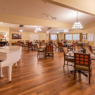 A spacious dining area featuring a white piano, wooden floors, and elegant chandeliers.