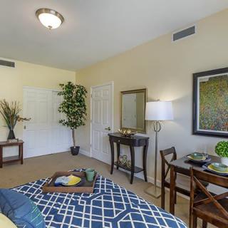A cozy bedroom with stylish decor, featuring a neatly made bed, a small table with chairs, and decorative plants.