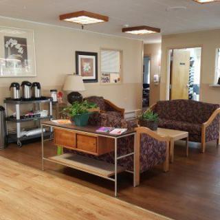 A cozy waiting room featuring comfortable seating, potted plants, a coffee station, and artwork on the walls.