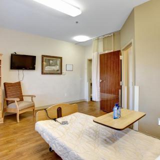A clean and well-lit hospital room with a bed, chair, television, and bedside table.