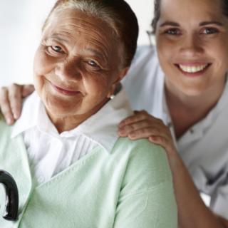 An elderly woman and a young woman smiling, showing care and support.