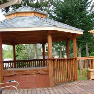 A wooden gazebo on a deck surrounded by trees, creating a peaceful outdoor setting.