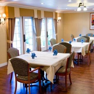 A well-lit dining room with neatly arranged tables and chairs, featuring elegant table settings and warm decor.