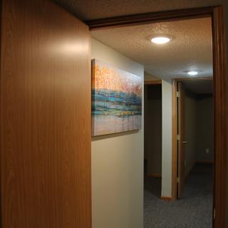 A dimly lit hallway with artwork on the wall and carpeted flooring.