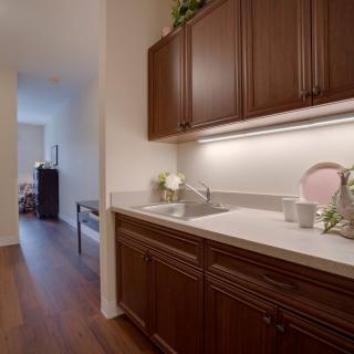 A modern kitchen area with wooden cabinets and a sink, leading into a hallway.