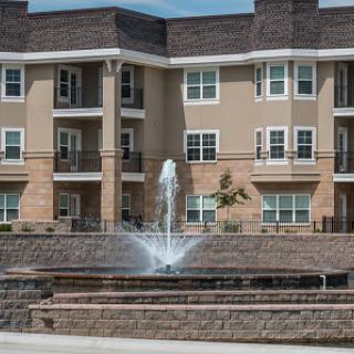 A modern residential complex featuring a decorative fountain in front.