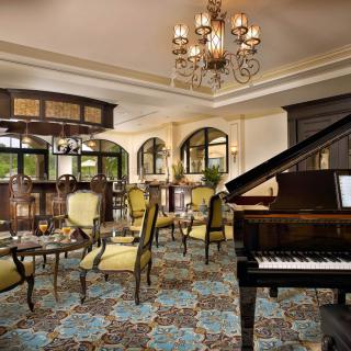 A luxurious lounge area featuring elegant armchairs, a grand piano, and a stunning chandelier.