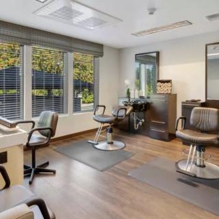 A modern salon interior featuring chairs and mirrors with large windows providing natural light.