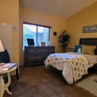 A cozy bedroom with a neatly made bed, decorated in warm tones and featuring a dresser by the window.