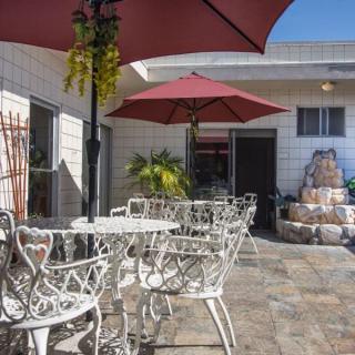 A sunny patio with wrought iron tables and chairs under red umbrellas.