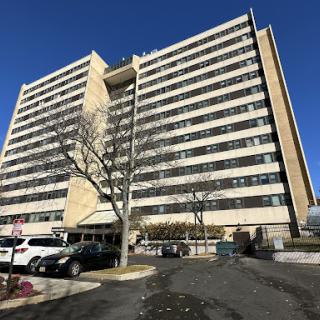 A residential apartment building with multiple floors and a parking area at the front.