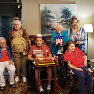 A group of elderly individuals celebrating with a cake and wearing party hats indoors.