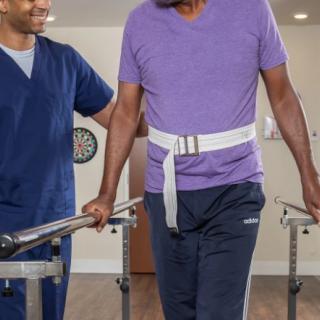 A healthcare professional assisting a person with rehabilitation exercises using parallel bars.