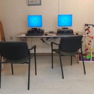 A small workstation with two computers and chairs in an office setting.
