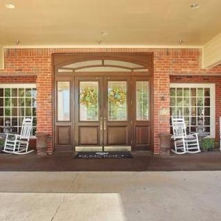 Entrance of a brick building with large wooden doors and rocking chairs on the porch.