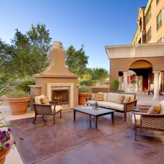 A beautifully furnished outdoor patio with a fireplace on a sunny day.