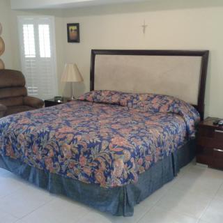 A cozy bedroom featuring a large bed with a floral comforter, a nightstand with a lamp, and an armchair in the corner.