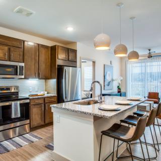 A modern kitchen with an island, featuring wood cabinets and stainless steel appliances.