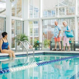 A serene indoor swimming pool scene with a woman relaxing by the water while a senior couple enjoys their time together.
