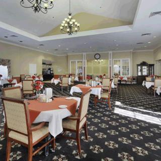 A spacious and elegantly decorated dining area with multiple tables, cushioned chairs, and chandeliers.