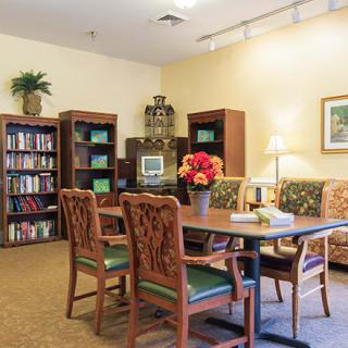A cozy library room featuring a table with chairs, surrounded by bookshelves and decorative items.