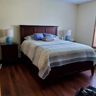 A cozy bedroom featuring a wooden bed with soft bedding, nightstands with lamps, and hardwood flooring.
