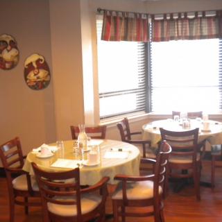 A cozy dining area with round tables, wooden chairs, and natural light streaming through the window.