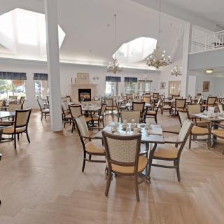 A spacious and bright dining room with elegantly set tables and chairs under decorative chandeliers.