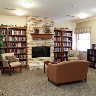 A cozy library with bookshelves, a fireplace, and comfortable seating.