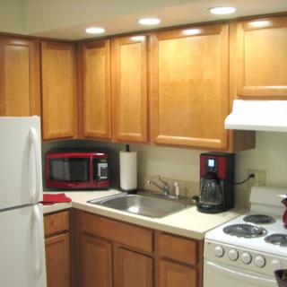 A compact, modern kitchen with wooden cabinets and various appliances including a refrigerator, microwave, coffee maker, stove, and sink.