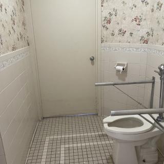A small bathroom with a tiled floor, floral wallpaper, and a toilet equipped with grab bars.