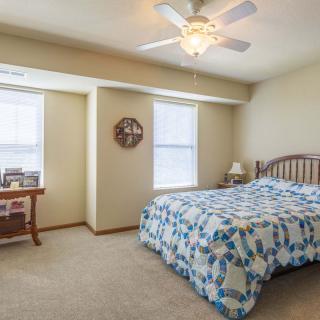 A cozy bedroom with a bed, ceiling fan, and natural light from windows.