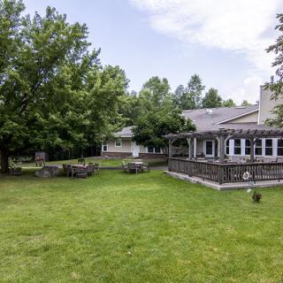 A serene backyard with a spacious lawn, surrounded by trees and featuring a house with a porch.