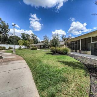 A peaceful outdoor scene with a grassy area, sidewalk, and buildings under a partly cloudy sky.