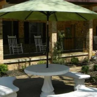 A cozy outdoor patio area with a round table and umbrella, surrounded by benches and rocking chairs.