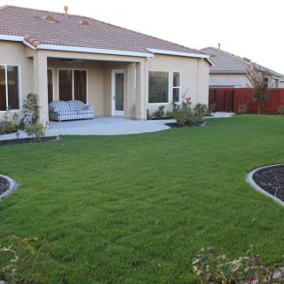 A backyard with a green lawn, patio area, and surrounding garden landscaping.