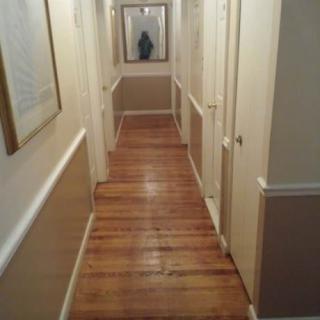 A narrow hallway with a wooden floor and a mirror at the end.