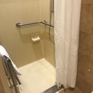 A clean and simple shower area featuring a white curtain and accessible design.