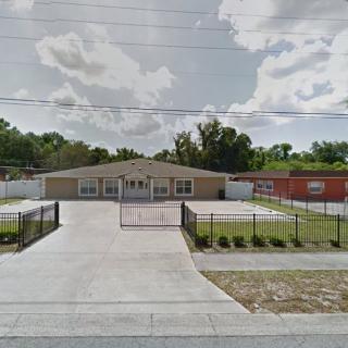 A building with a gated driveway and fenced yard under a cloudy sky.