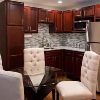 A modern kitchen with dark wood cabinets, stainless steel appliances, and a cozy dining area featuring a glass table and upholstered chairs.