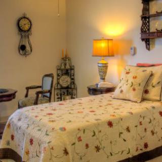 A cozy bedroom with a single bed dressed in floral bedding, illuminated by a warm lamp alongside decorative vintage clocks.