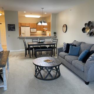 A cozy open-plan living room with a kitchen and dining area, furnished with a comfortable sofa, coffee table, and dining set.