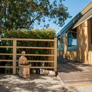 A sunny garden area with a wooden fence and a small statue, adjacent to a modern house.