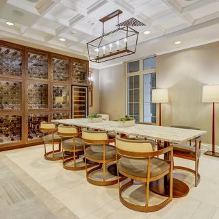 A modern dining room with a large table, stylish chairs, and an elegant chandelier, featuring a wall-mounted wine rack.