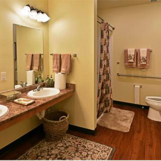 A warmly decorated bathroom with dual sinks, a shower curtain, and wooden flooring.