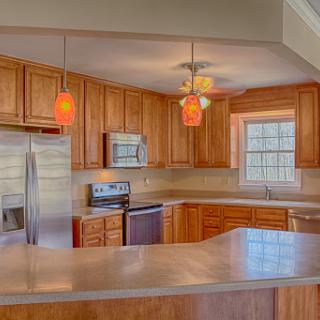 A sleek and modern kitchen featuring wooden cabinetry and stainless steel appliances, illuminated by stylish pendant lights.