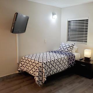 A modern bedroom with a single bed, wall-mounted TV, and bedside lamp.