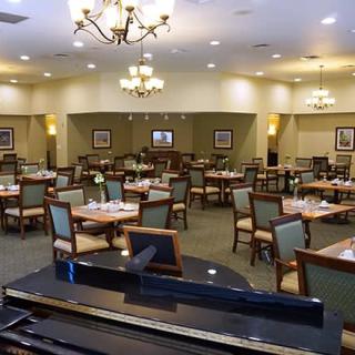 An elegantly decorated restaurant dining room with empty tables, a piano, and chandeliers.