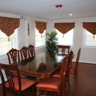 A dining room with a wooden table and chairs, decorated with curtains and a potted plant.